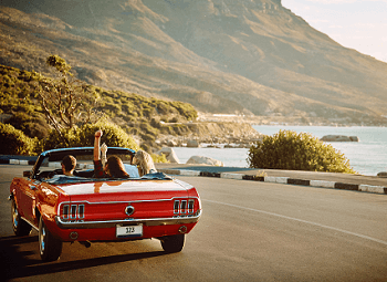 Three people in an older red convertible driving down the freeway on the coast